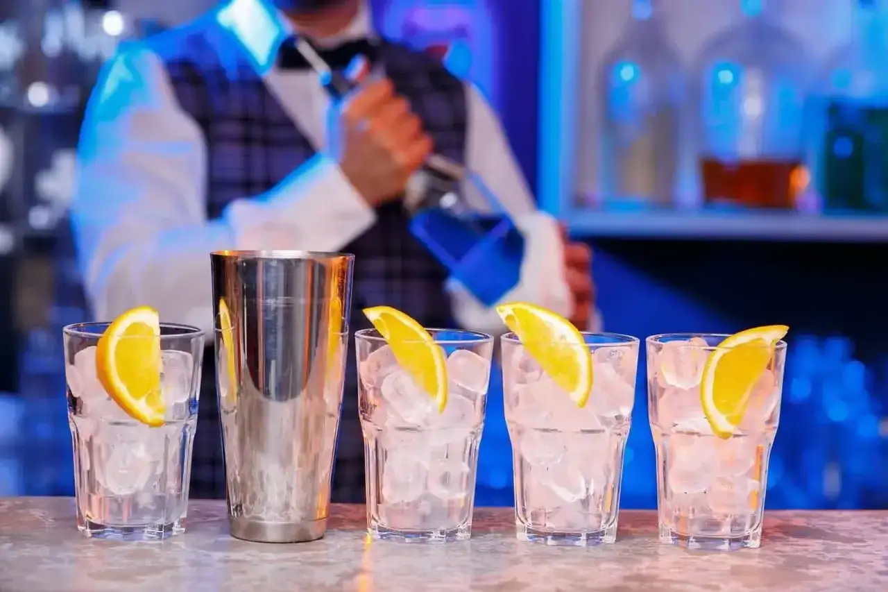 Barman przygotowuje drinki. Zastanawiasz się, ile kosztuje kurs barmanski? Zobacz, jak powstają drinki z lodem i pomarańczą.