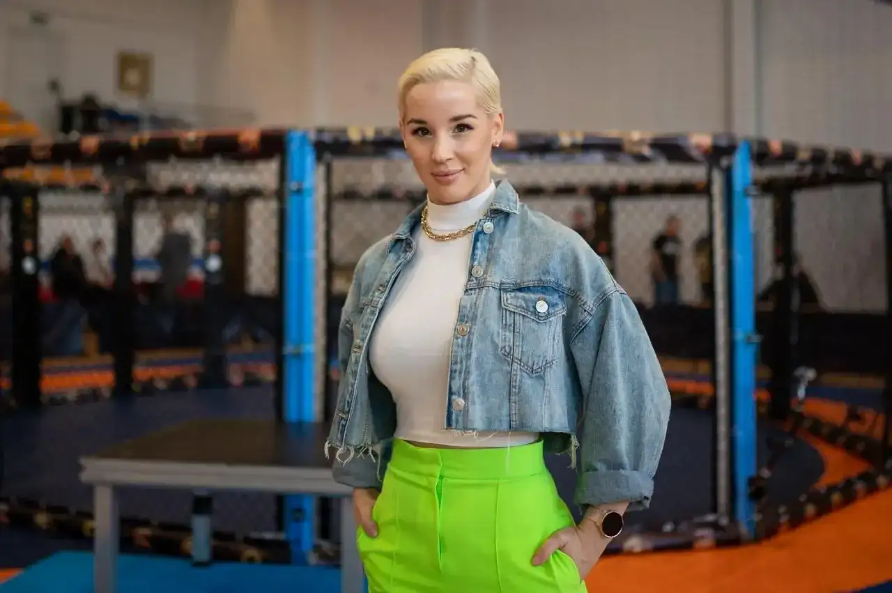 Kobieta w dżinsowej kurtce i neonowych spodniach stoi przed klatką MMA. Ile lat ma Aniela Bogusz?