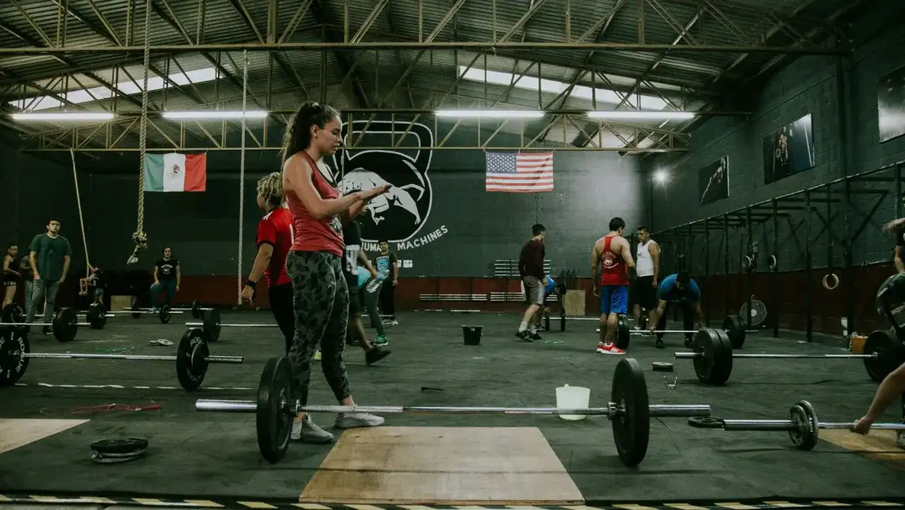 Ludzie ćwiczący CrossFit w siłowni z ciężarami i flagami Meksyku i USA.