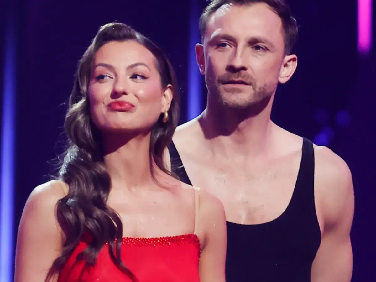 Kamil Nożyński i jego partnerka, w czerwonej sukni i czarnym topie, prezentują się na scenie.
