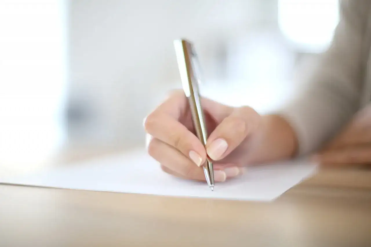 Main d'une personne écrivant avec un stylo sur un document.