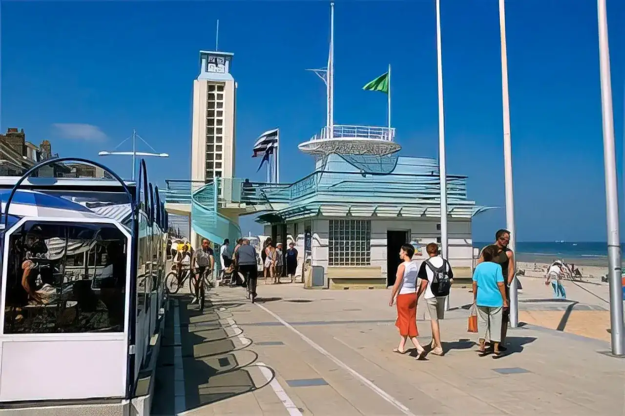 Promenade de Malo-les-Bains avec tramway, tour, bâtiments bleus et baigneurs sur la plage.