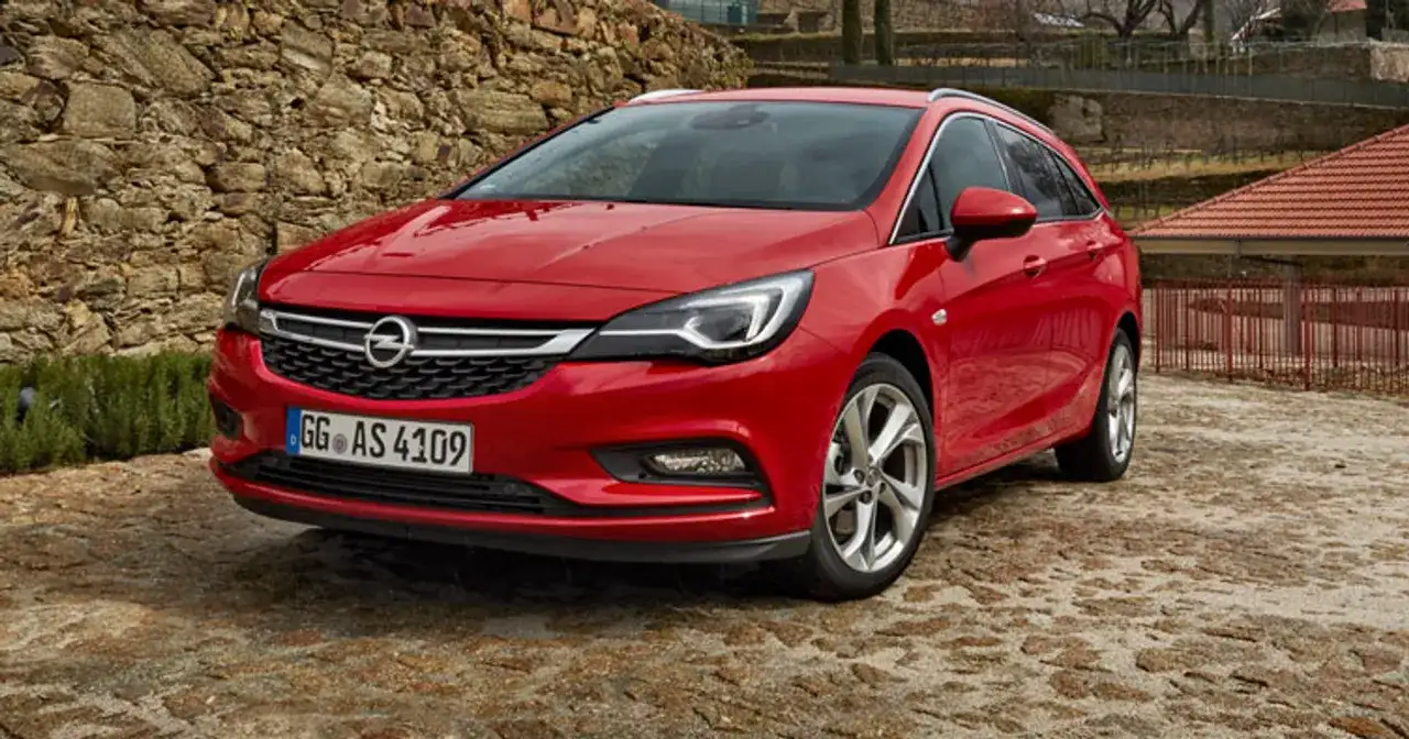 Czerwony Opel Astra Sports Tourer zaparkowany na kamienistej nawierzchni, z kamiennym murem w tle.