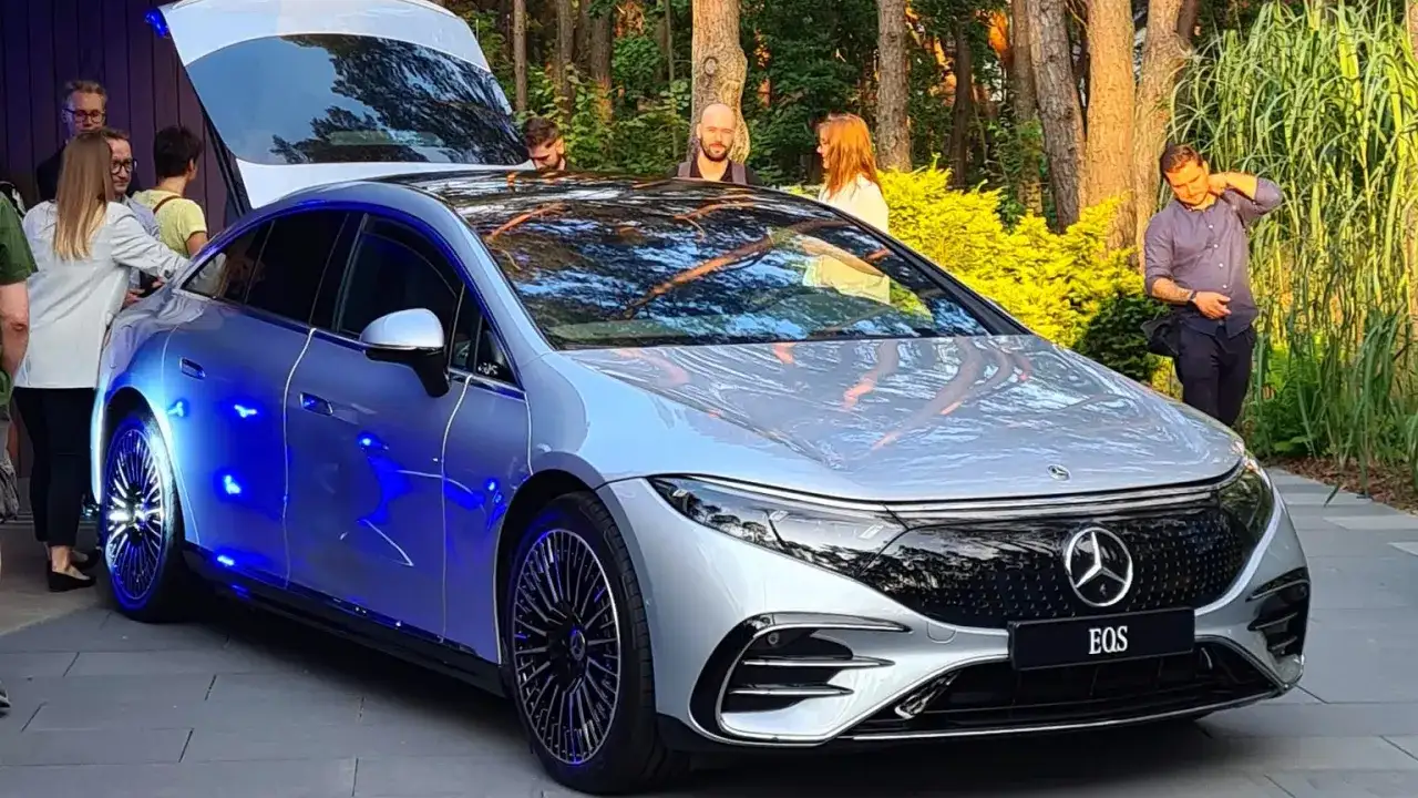 Srebrny Mercedes EQS z niebieskim podświetleniem prezentuje się efektownie na tle zieleni.