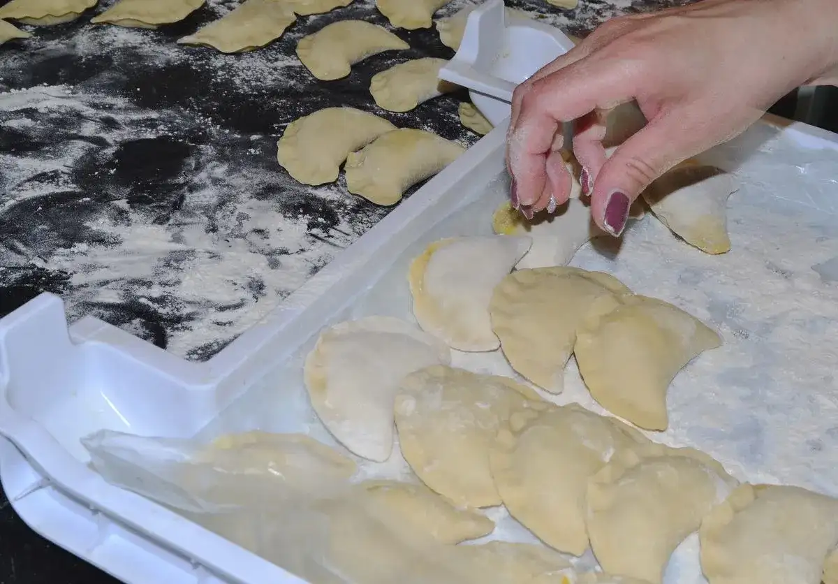 Ręka układa pierogi na tacy, posypanej mąką. Aby ugotowane pierogi się nie skleiły, warto je od razu po ugotowaniu delikatnie polać tłuszczem.