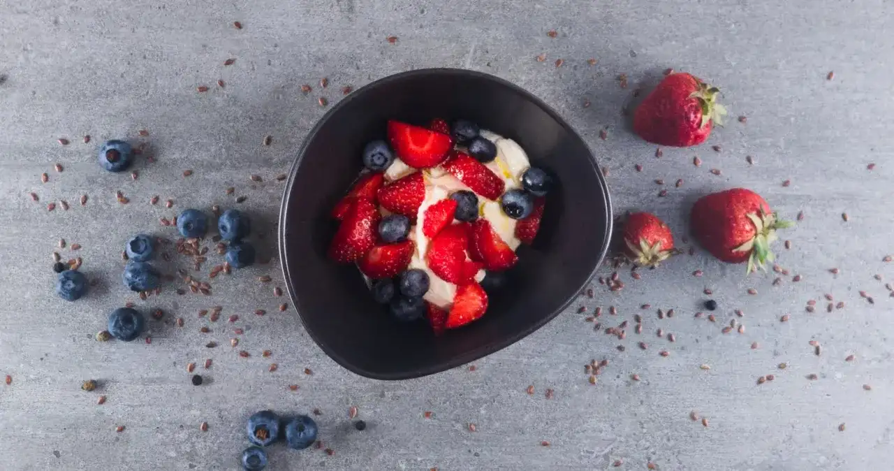 Schüssel mit cremigem low carb Joghurt, garniert mit frischen Erdbeeren und Blaubeeren. Leinsamen verstreut.