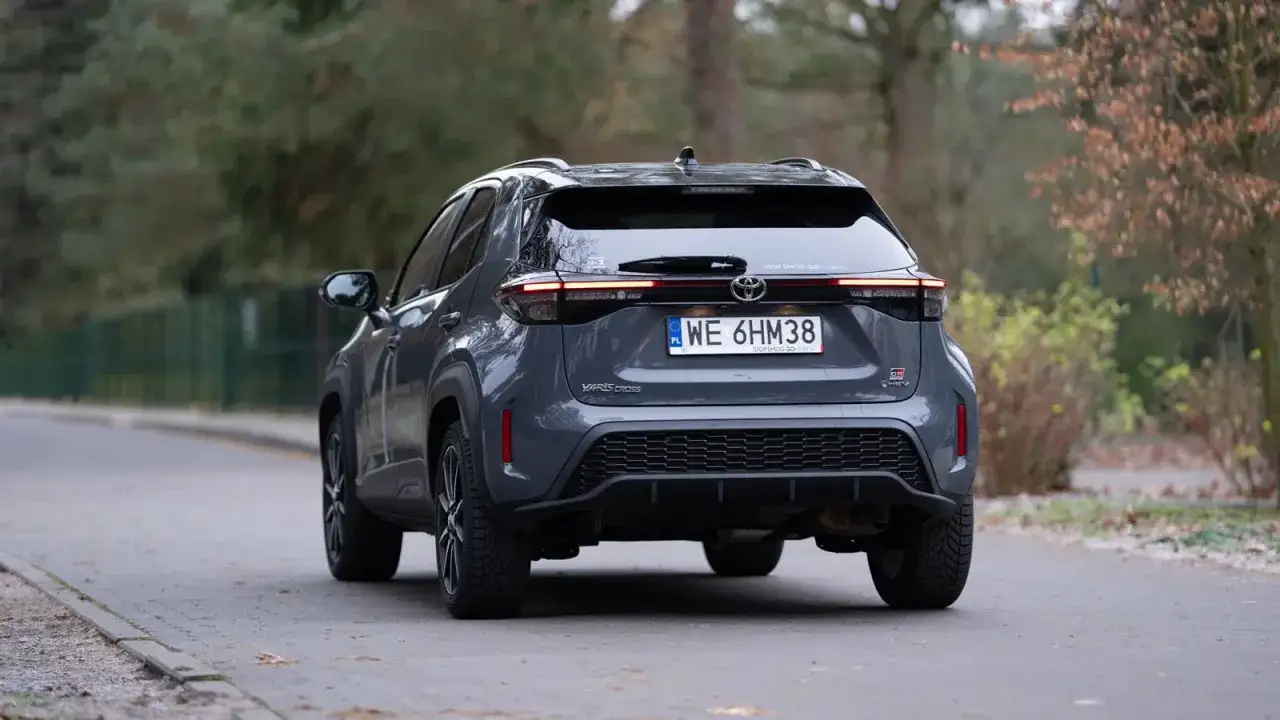 Szary Toyota Yaris Cross hybrydowy z tyłu na drodze.