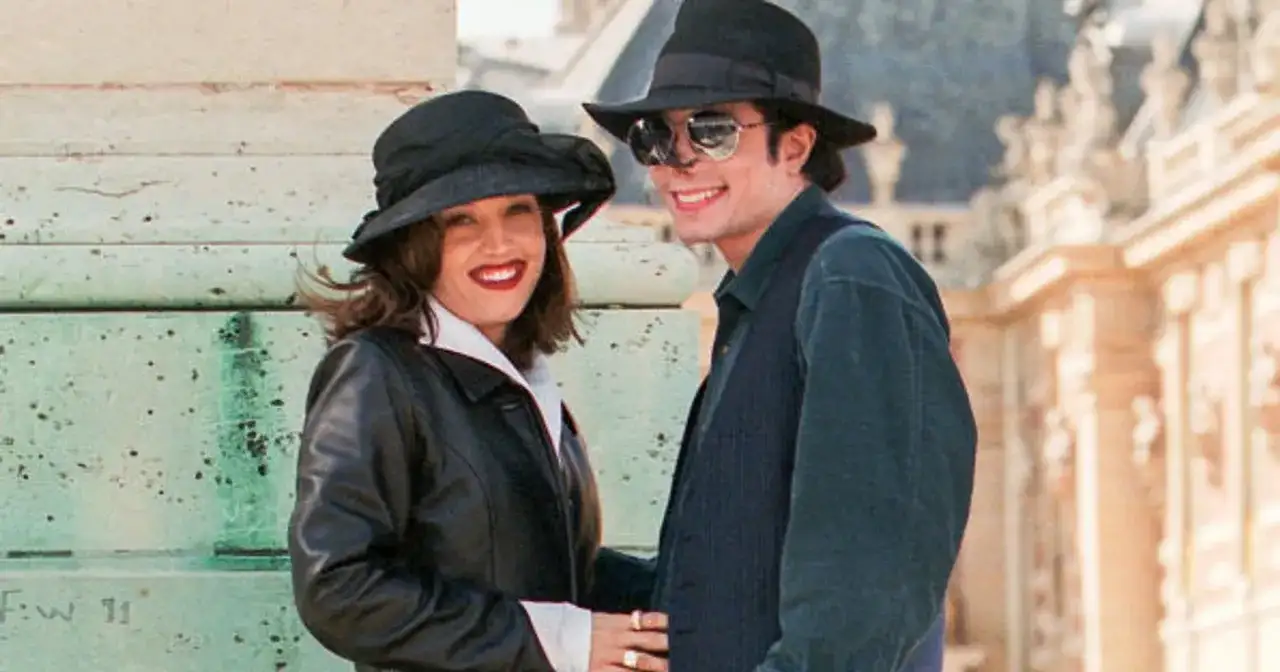 Lisa Marie Presley i jej mąż Michael Jackson w kapeluszach i okularach przeciwsłonecznych, uśmiechnięci na tle budowli.