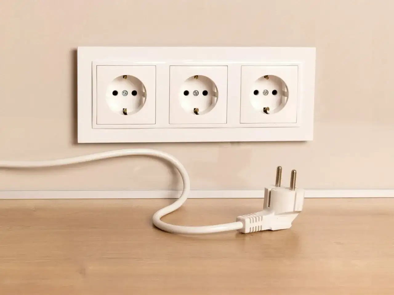 Biały kabel z wtyczką leży na drewnianym blacie, obok gniazdek elektrycznych w ścianie.