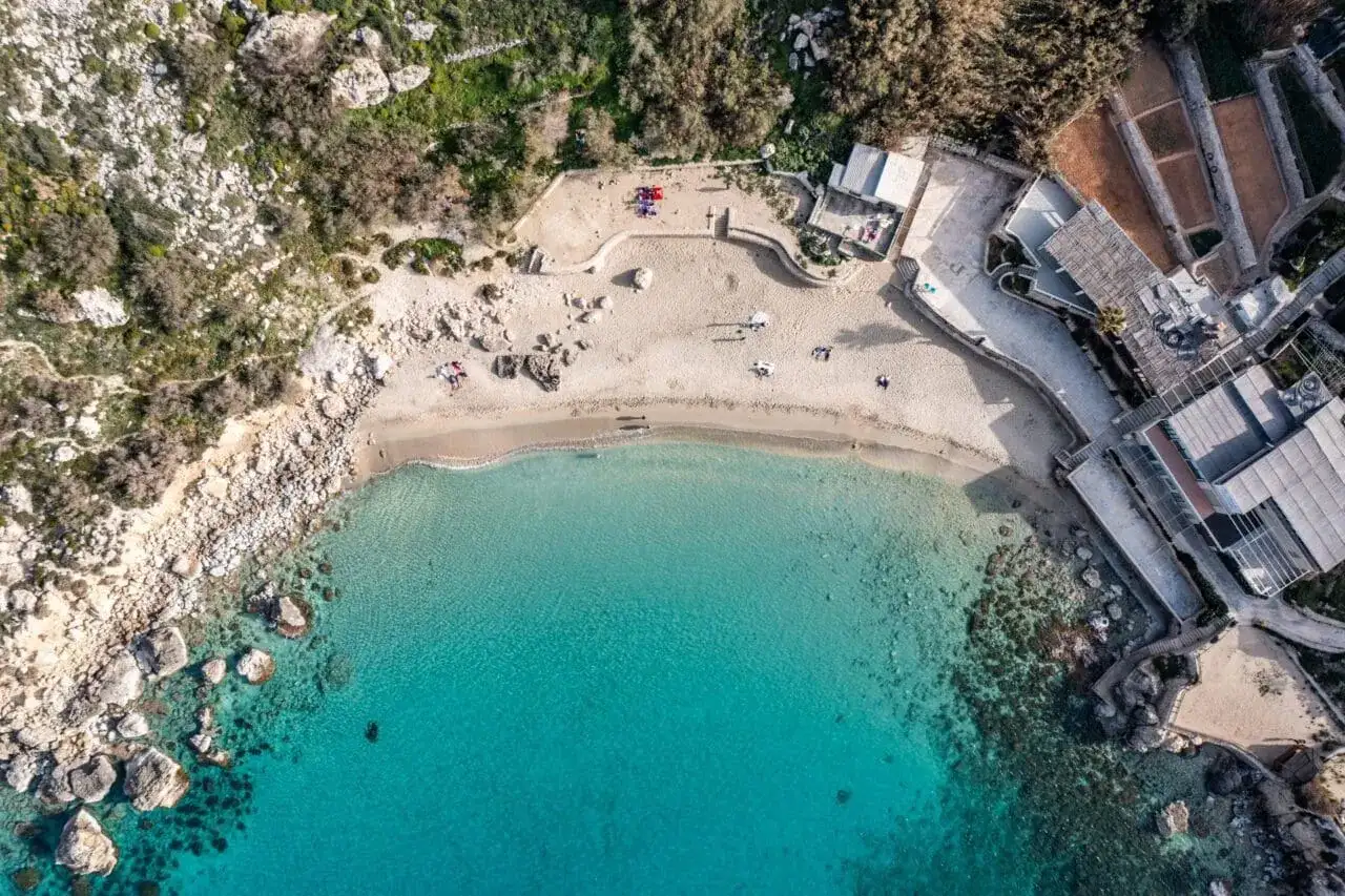 Malta: piaszczyste plaże otoczone skałami i zielenią, z turkusową wodą i kilkoma osobami odpoczywającymi na piasku.