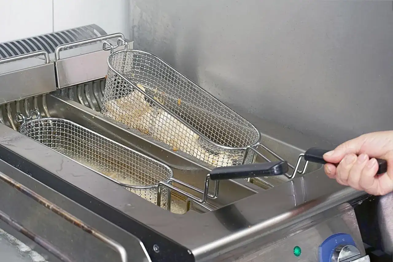 Frytki smażące się w metalowych koszach we frytkownicy.