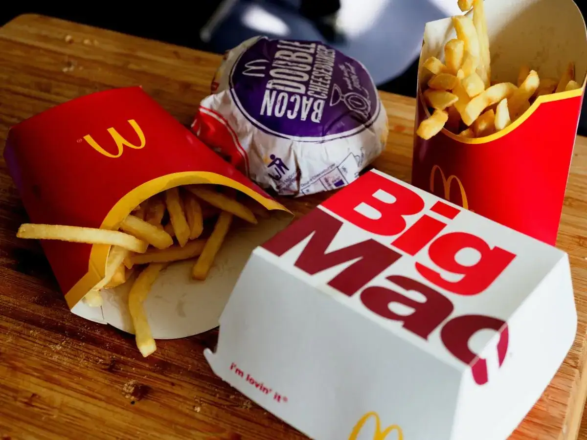 Frytki z McDonald's w czerwonych opakowaniach obok pudełka Big Mac i burgera.