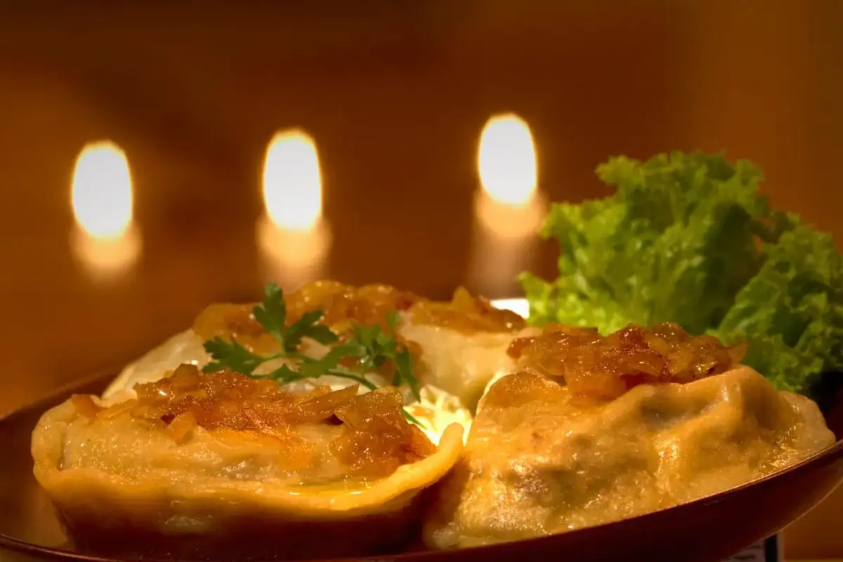 Pierogi z cebulką i natką pietruszki, podane z sałatą, na tle świec.