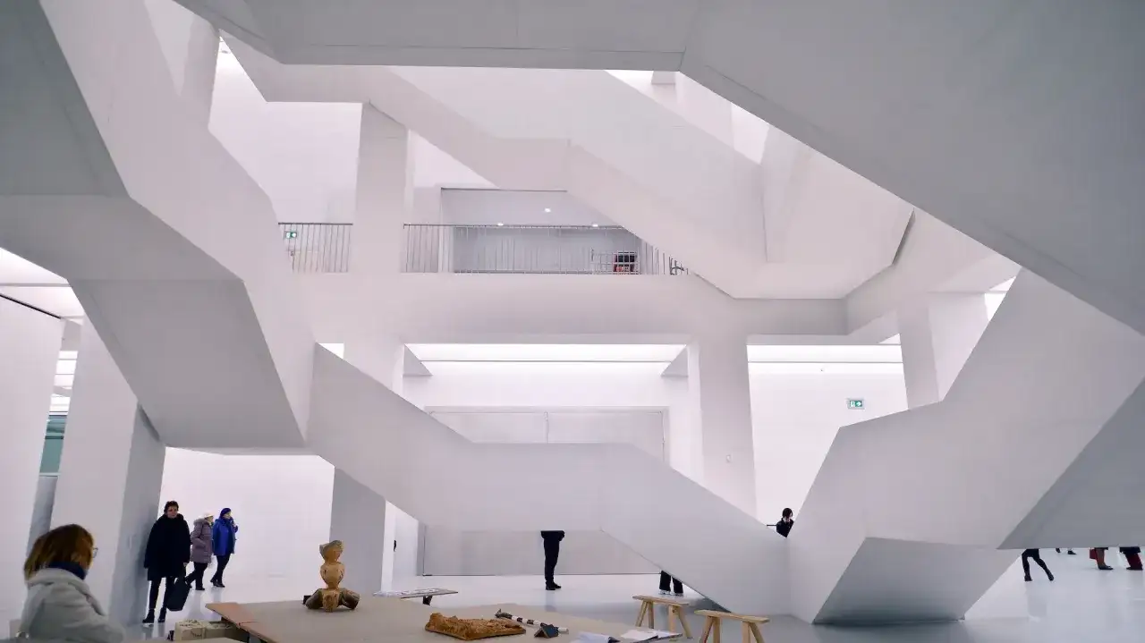 Nowoczesne muzeum sztuki z białymi, geometrycznymi schodami i kilkoma zwiedzającymi.
