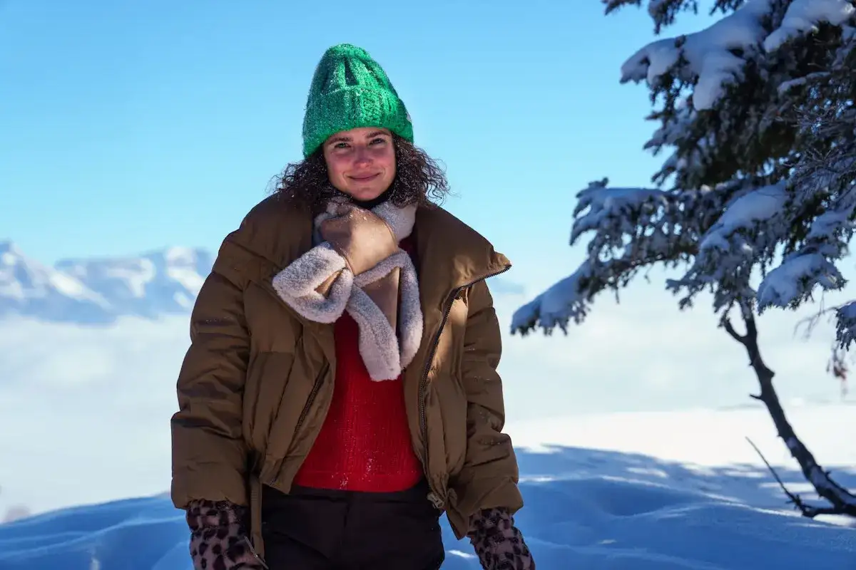 Frau mit grüner Strickmütze und brauner Winterjacke im Schnee.