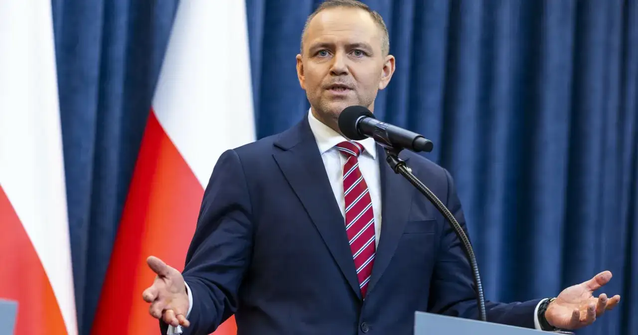 Mężczyzna w garniturze przemawia przy mikrofonie na tle flagi Polski. Czy prezydent faktycznie planuje ogłosić stan wyjątkowy w związku z sytuacją na wschodzie?