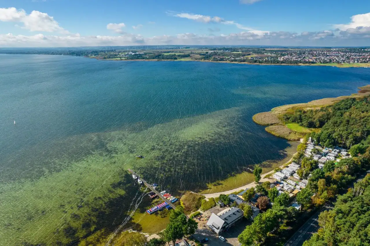Widok z lotu ptaka na zatokę z pomostem, łodziami, kempingiem i lasem.