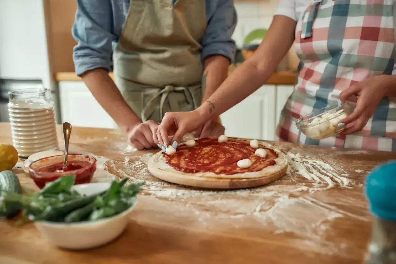 Para pysznej pizzy w piekarniku z termoobiegiem. Dwie osoby przygotowują pizzę, dodając mozzarellę.