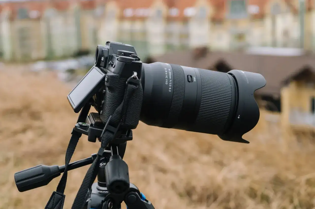 Aparat fotograficzny z obiektywem 18-300mm na statywie, z rozmytym budynkiem w tle.