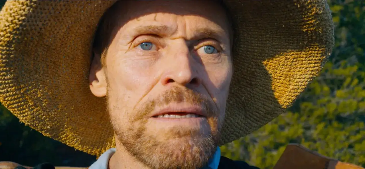 Willem Dafoe jako Van Gogh u Bram Wieczności, z niebieskimi oczami i słomkowym kapeluszem, wpatruje się w dal.