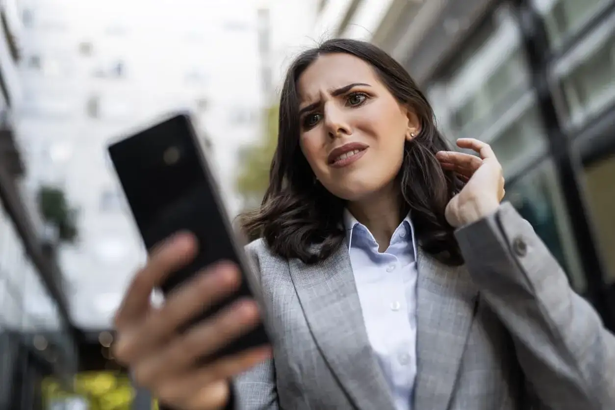 Zmartwiona kobieta próbuje odzyskać hasło do FB, patrząc na telefon.