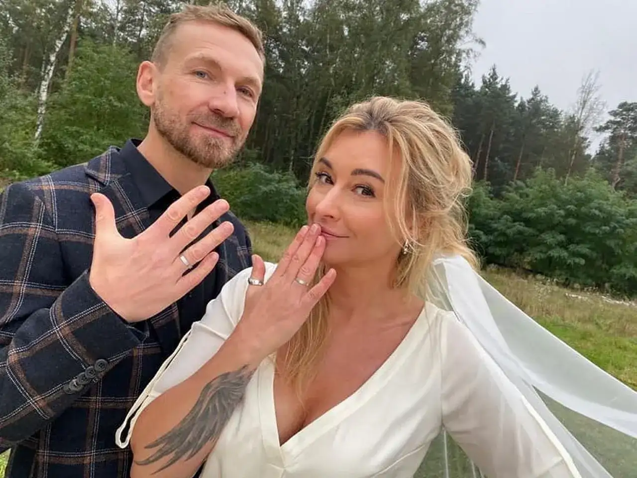 Martyna Wojciechowska i Kossakowski pokazują obrączki. Uśmiechnięci, w plenerze, świętują ważny moment.