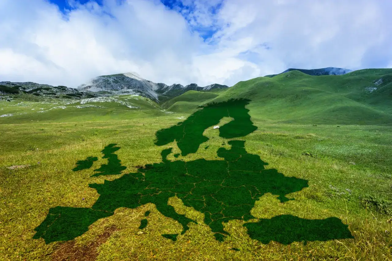 Mapa Europy w kształcie zielonej trawy na tle gór i błękitnego nieba.