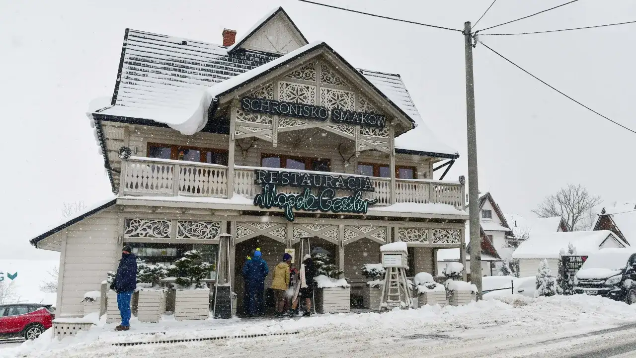 Drewniana restauracja "Schronisko Smaków" w Bukowinie Tatrzańskiej, pokryta śniegiem, z neonem "Restauracja".