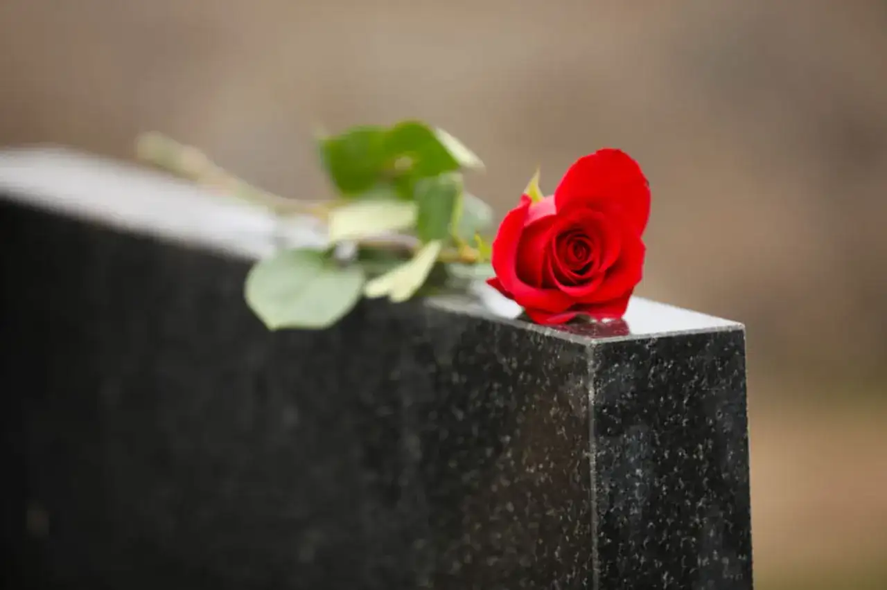 Une rose rouge sur une pierre tombale, symbole de deuil et de souvenir. Le notaire s'occupe du déblocage des fonds succession.