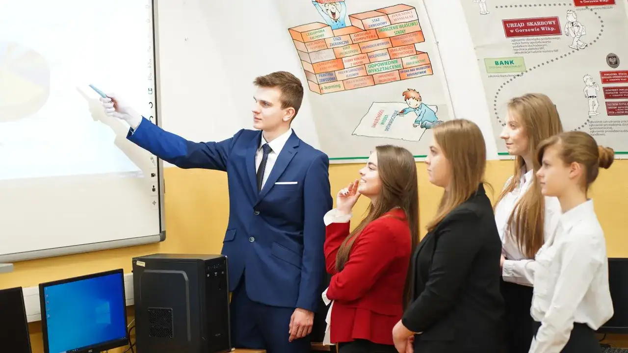 Młody technik ekonomista tłumaczy wykres na tablicy interaktywnej grupie uczniów.