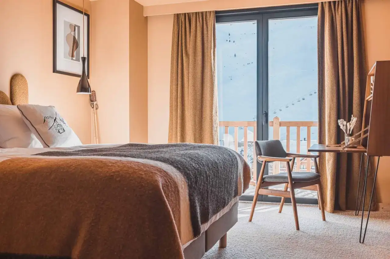 Chambre d'hôtel avec lit douillet, vue sur les montagnes enneigées et télécabines.