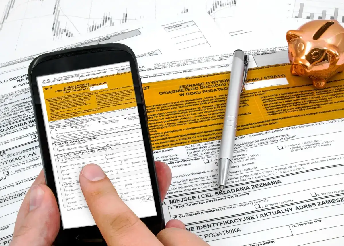 Smartfon z formularzem PIT-37 i złotą świnką skarbonką. Instrukcja jak rozliczyć PIT 37.