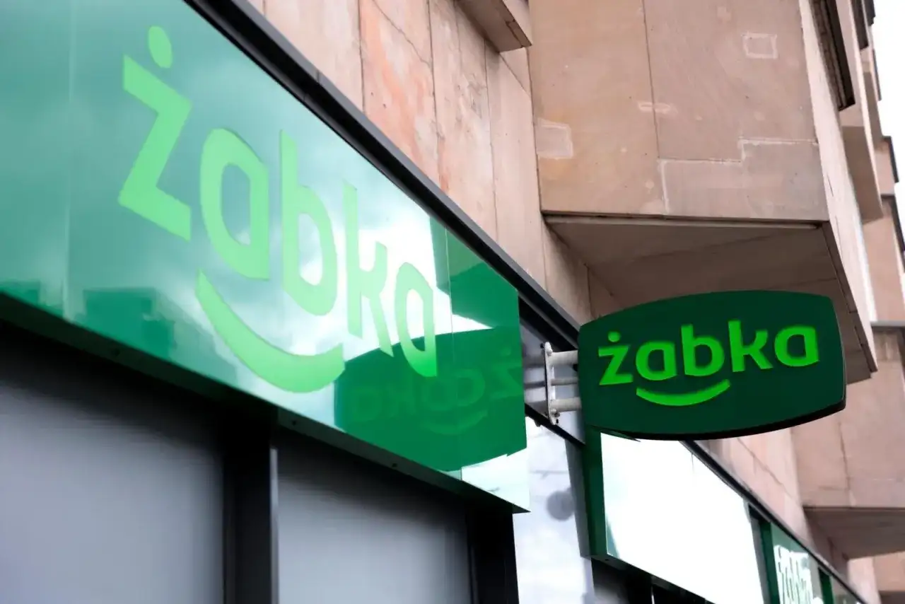 Zielony neon z logo Żabki. Zastanawiasz się, od ilu lat można pracować w Żabce? Odpowiedź znajdziesz w tym sklepie.