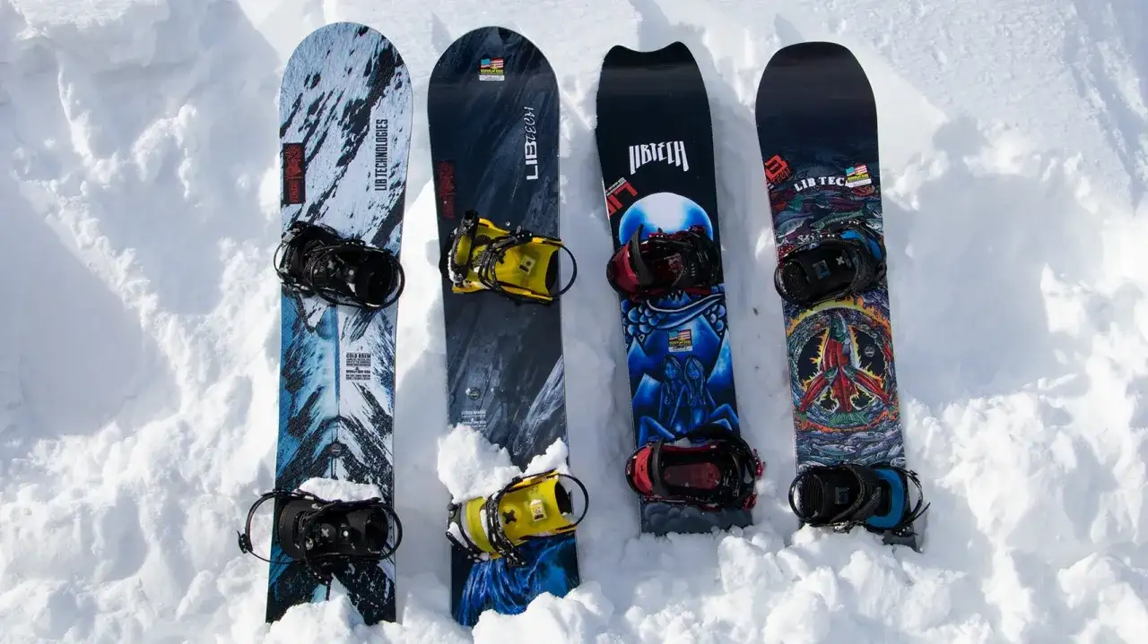 Cztery deski snowboardowe z różnymi grafikami i wiązaniami, leżące na śniegu.