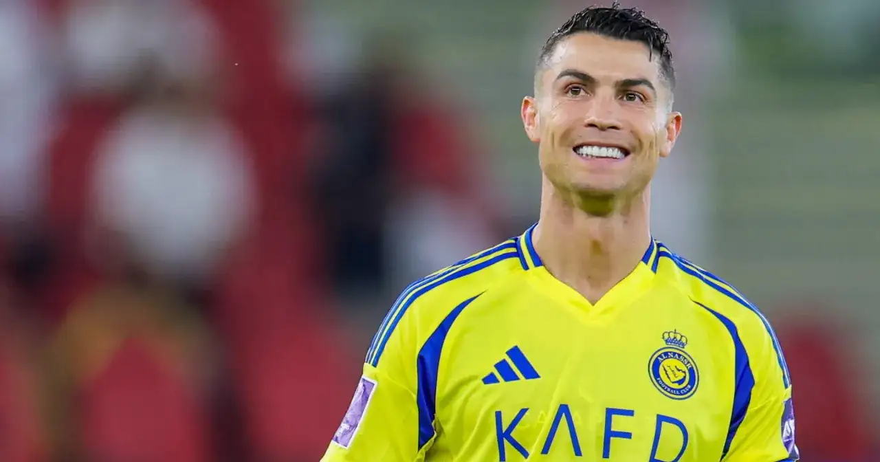 Uśmiechnięty Cristiano Ronaldo w żółtej koszulce z niebieskimi pasami, grający w klubie Al Nassr.
