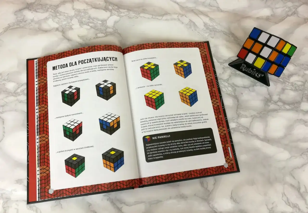 Otwarta książka z instrukcją jak ułożyć kostkę Rubika. Pokazuje etapy układania białej ściany i krawędzi.