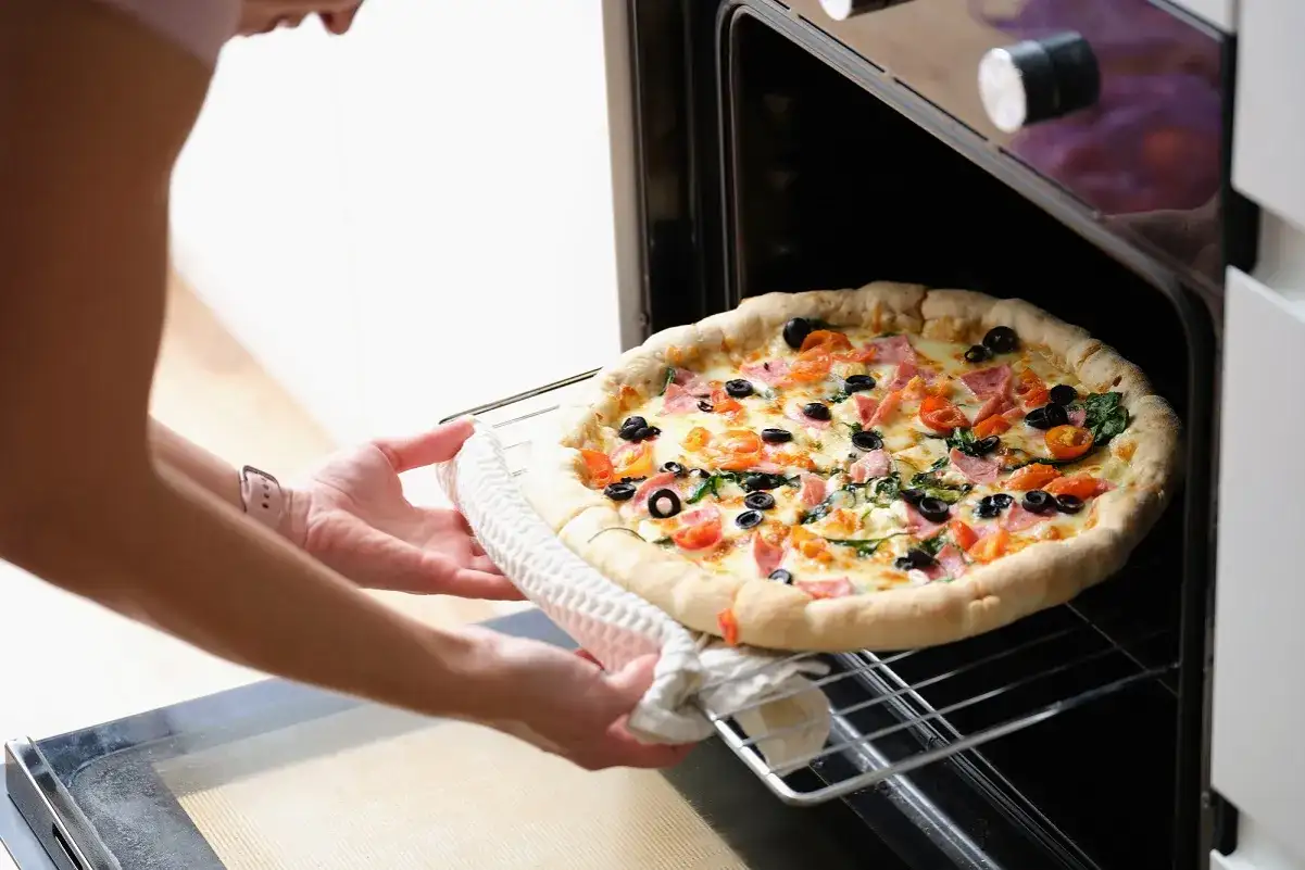Ręce wkładają pizzę do piekarnika. Zastanawiasz się, ile czasu piec pizzę, by była idealna?