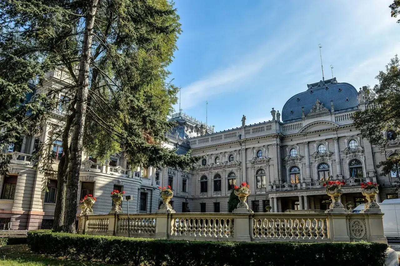 Majestatyczny pałac poznański z ozdobną balustradą i kwitnącymi kwiatami, otoczony zielenią.