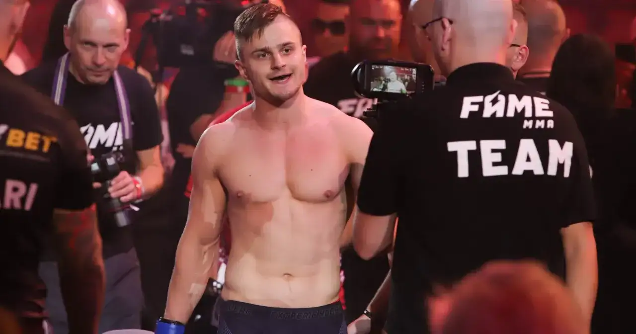 Amadeusz Ferrari, zawodnik MMA, wychodzi na ring, otoczony przez ekipę i kamery.