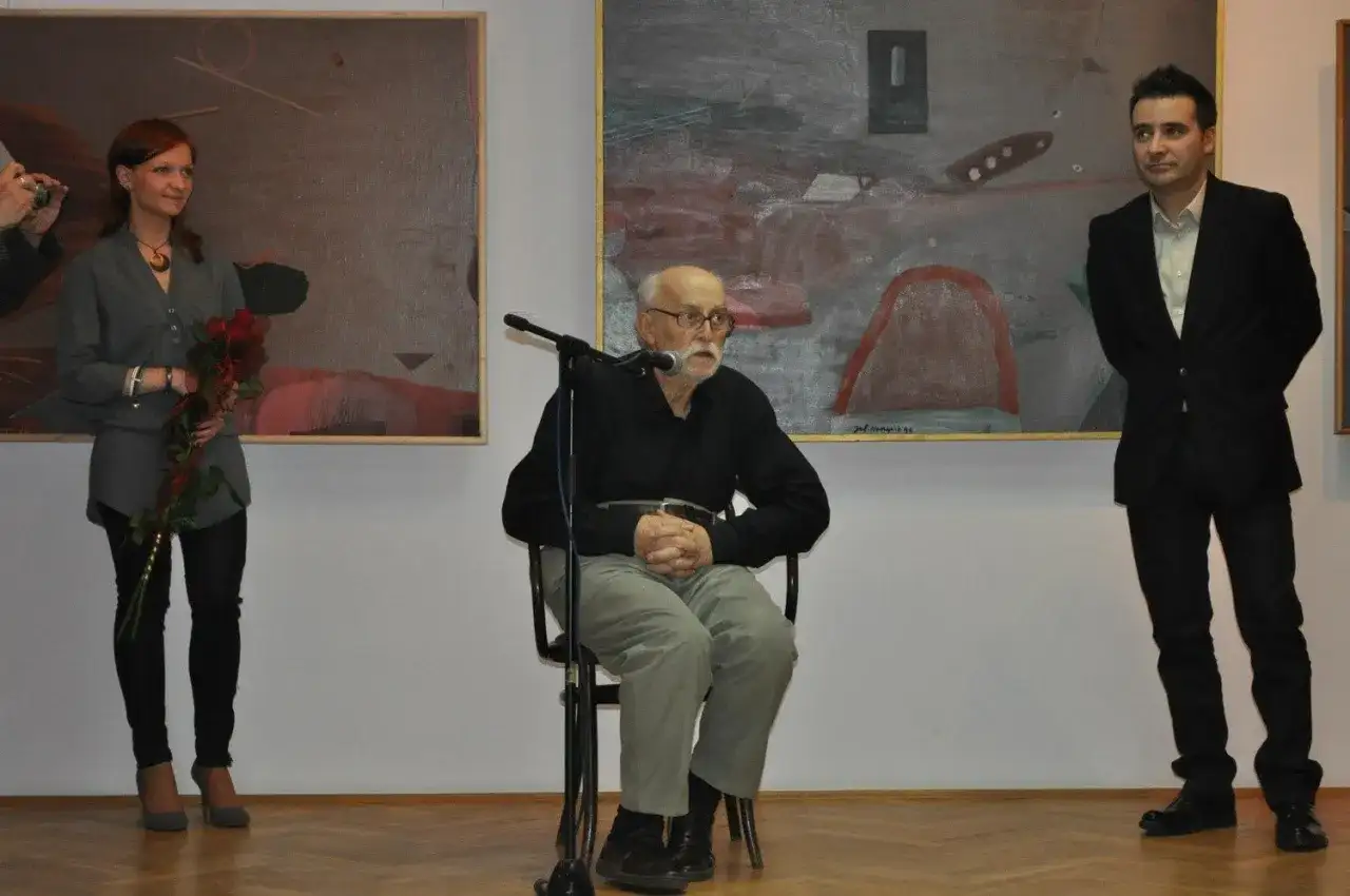 Konrad Wieniawa-Narkiewicz siedzi przy mikrofonie, obok niego stoi kobieta z kwiatami i mężczyzna w garniturze.