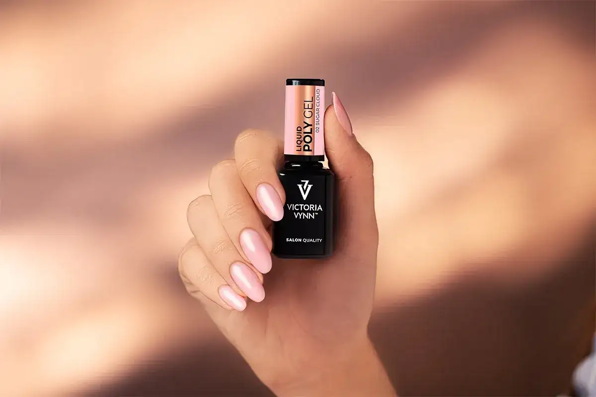 Dłoń z różowymi paznokciami trzyma buteleczkę Liquid Poly Gel Victoria Vynn. To produkt do stylizacji paznokci.