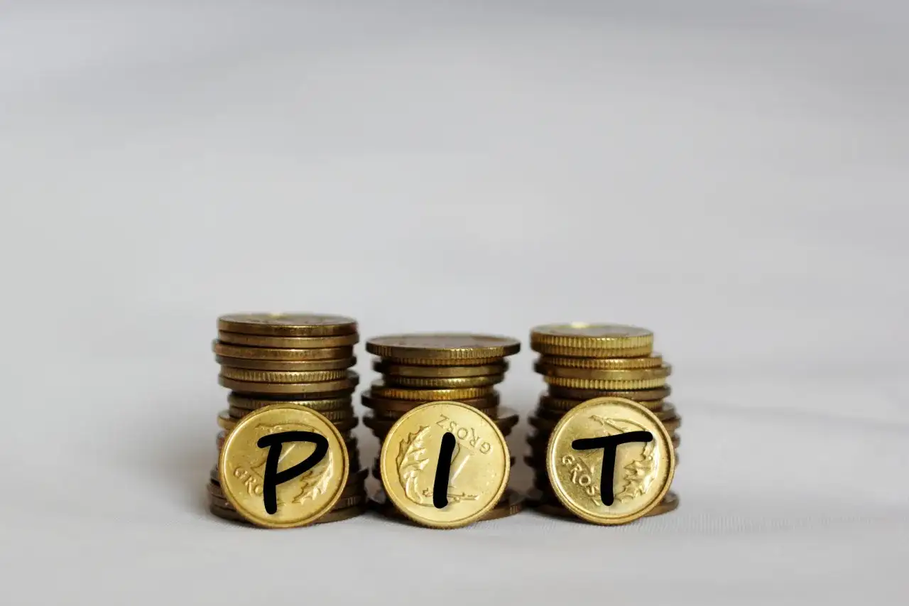 Trzy stosy monet, na których widnieją litery P, I, T. Symbolizują one rozliczenie podatku PIT.