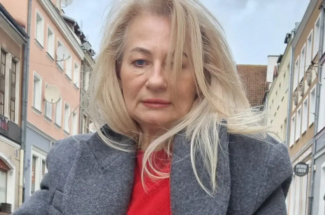 Szafiarka Dorka, ile ma lat? Kobieta w szarym płaszczu i czerwonym swetrze na tle kamienic.