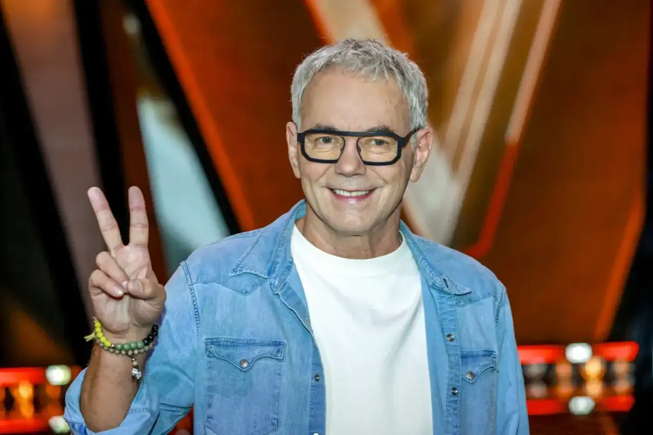 Robert Janowski, syn księdza, w dżinsowej koszuli i okularach, pokazuje znak pokoju.