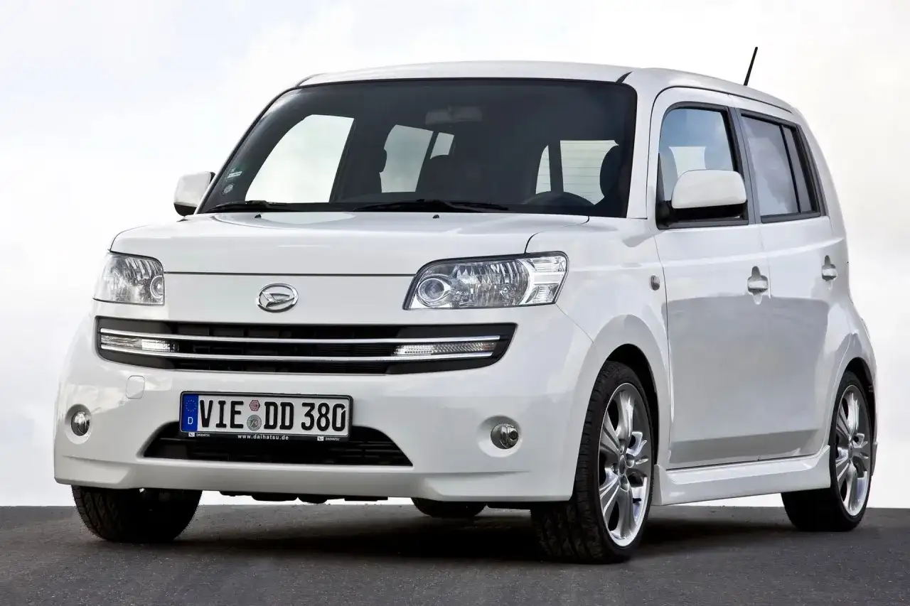 Biały Daihatsu Materia z niemieckimi tablicami rejestracyjnymi stoi na ciemnej nawierzchni.