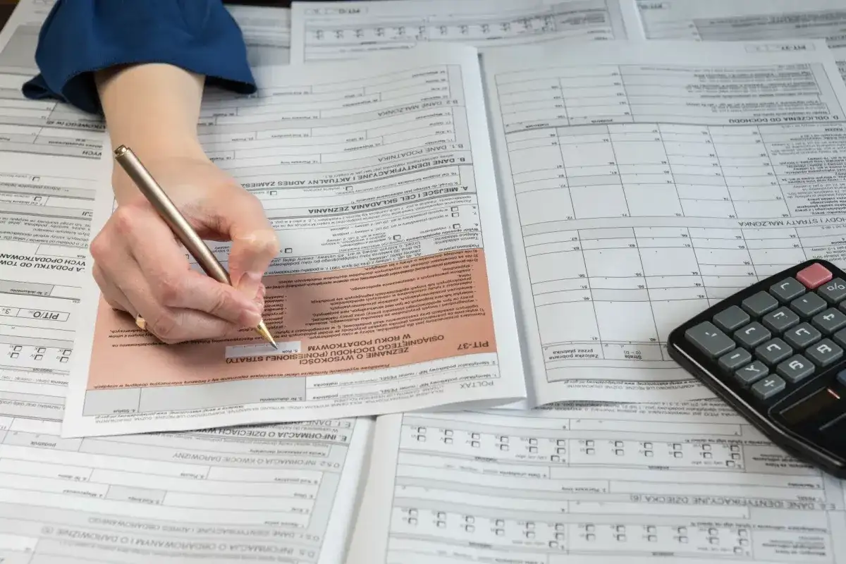 Ręka z długopisem wypełnia formularz PIT-37, obok leży kalkulator. To pomoc w rozliczeniu PIT 36.