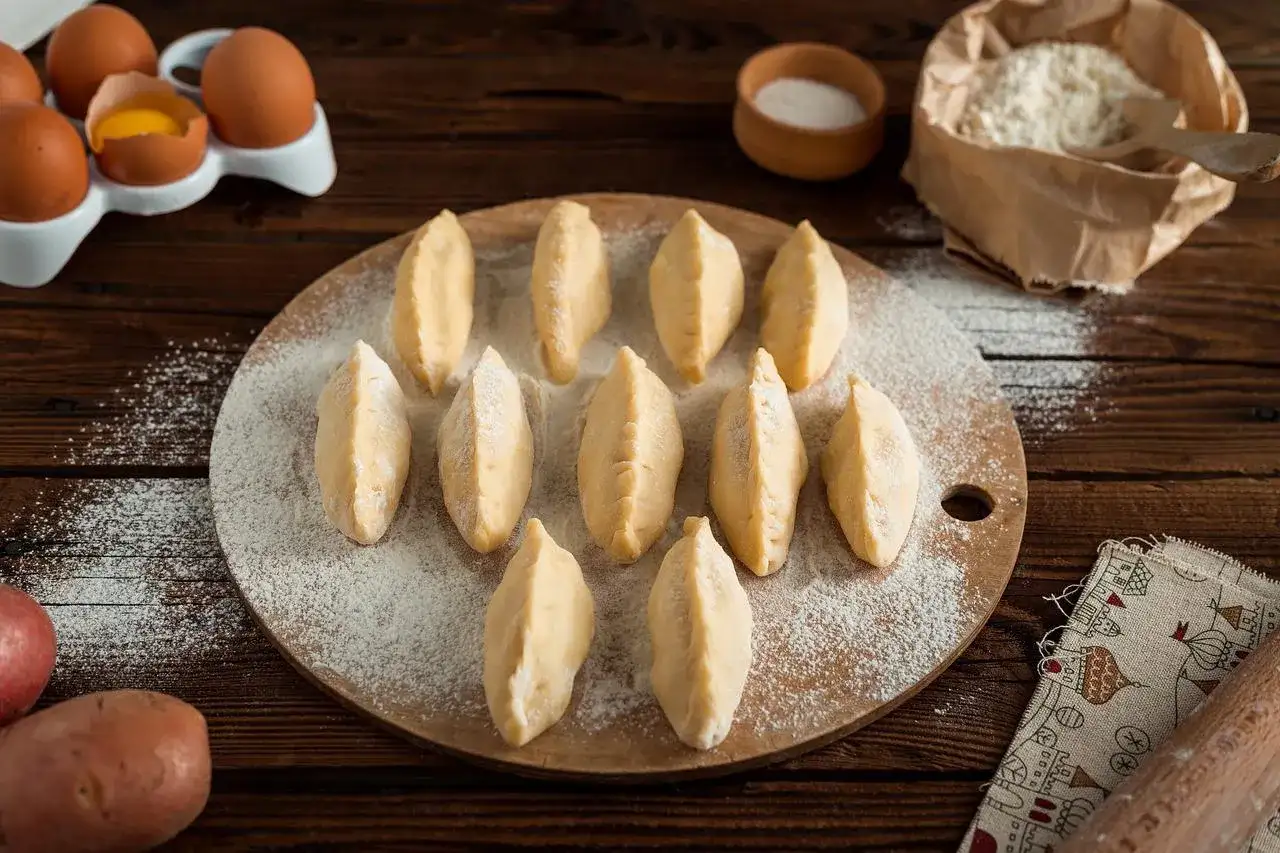 Gotowe do lepienia pierogi na desce, obok jajka i mąka. Czy ciasto na pierogi można zamrozić? Tak, to świetny sposób na zapas!