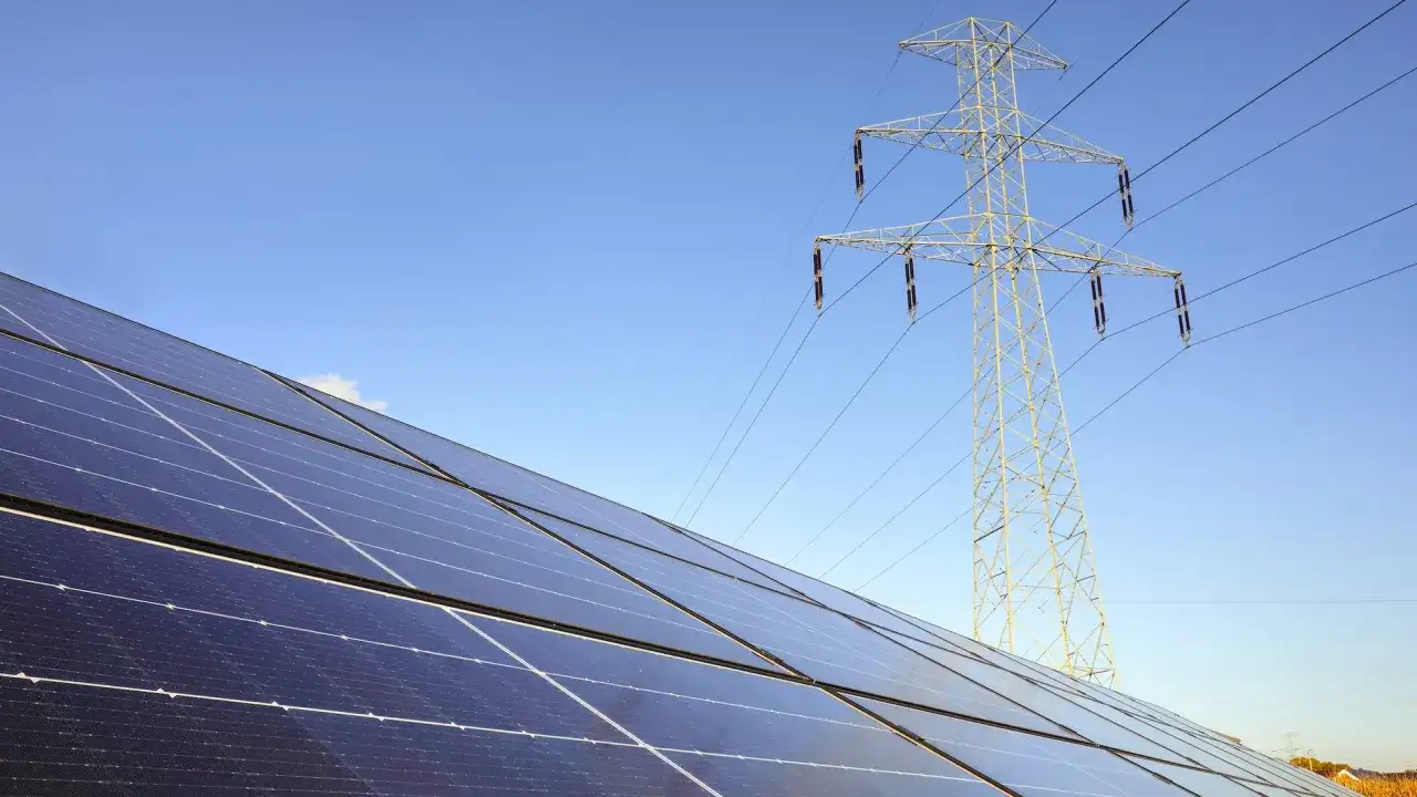 Panele fotowoltaiczne i linia energetyczna pod błękitnym niebem. Zastanawiasz się, jak zresetować fotowoltaikę?