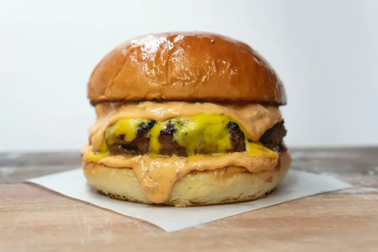 Soczysty burger z roztopionym serem i sosem na jasnym tle.
