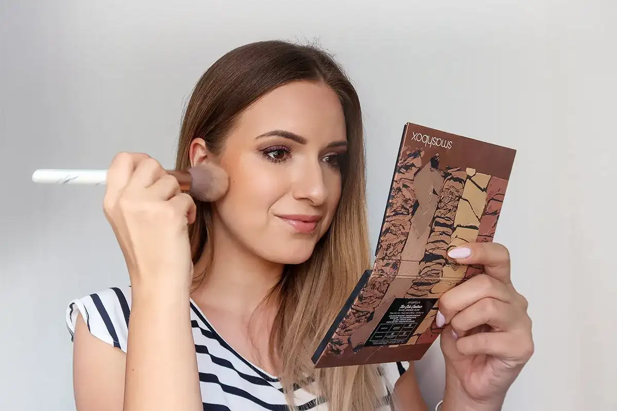 Kobieta nakłada puder pędzlem, trzymając w dłoni paletkę do konturowania. Efekt subtelnego makijażu no makeup.